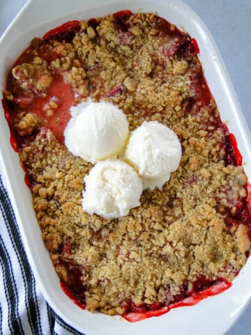 Strawberry crumble in white rectangle baking dish with 3 scoops of vanilla ice cream in center.