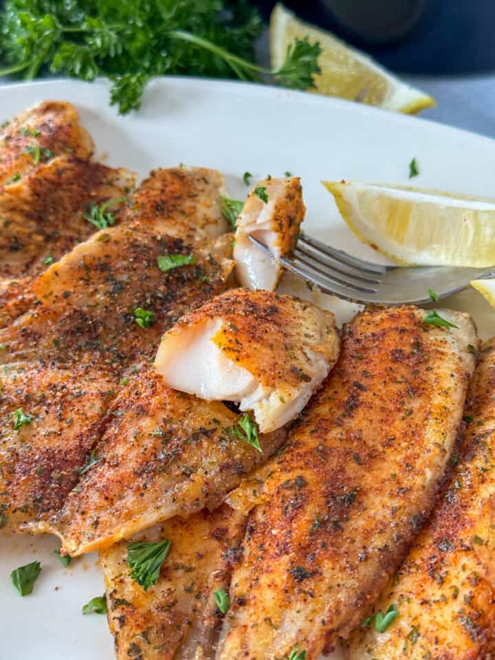 Air fryer tilapia on serving plate with bite on fork.