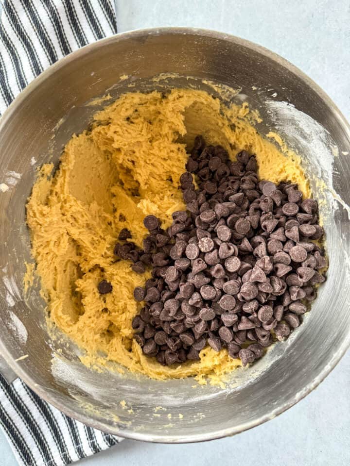 Chocolate chips added to cookie dough in large mixing bowl.