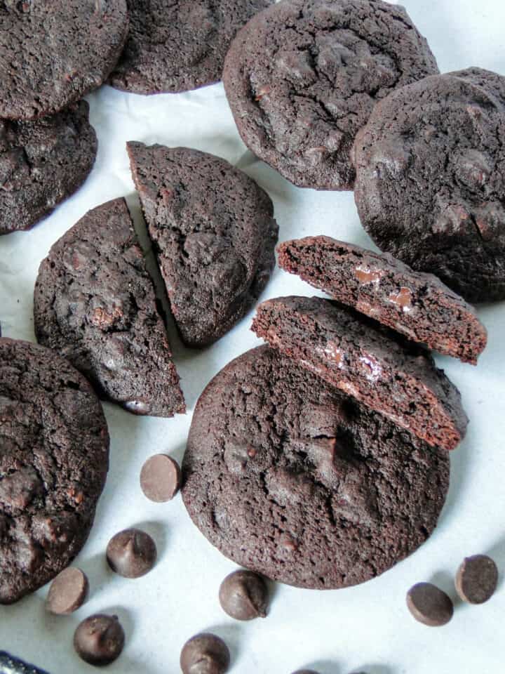 Closer top view of double dark chocolate chip cookies in a pile with two cookies cut in half showing chewy centers.