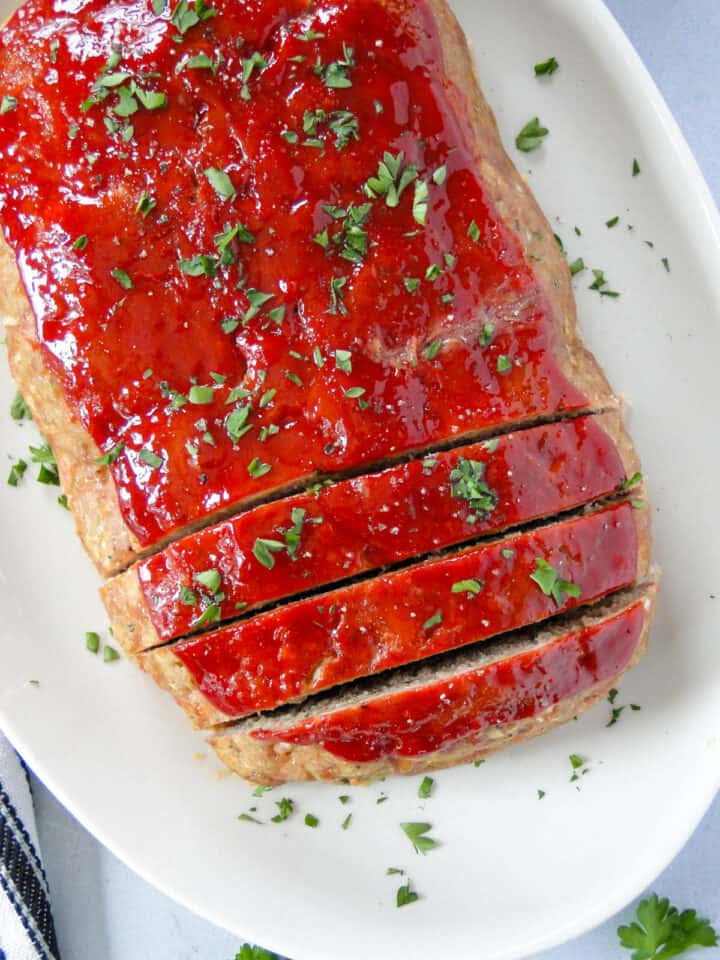 Top view of easy turkey meatloaf on white oval platter with 3 slices cut.
