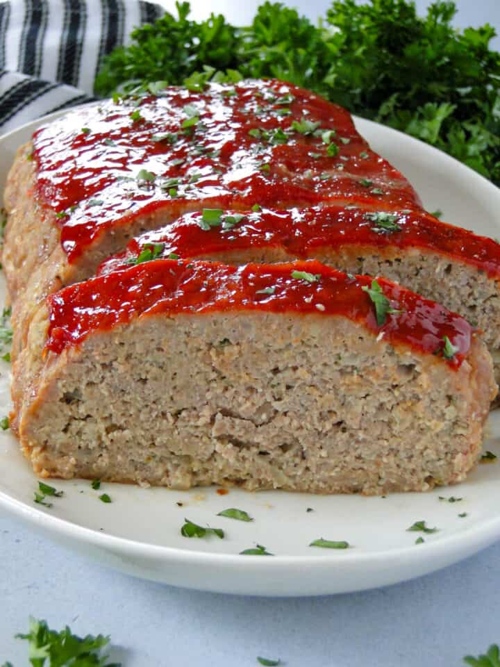 Close up side view of easy turkey meatloaf slice on white oval platter.