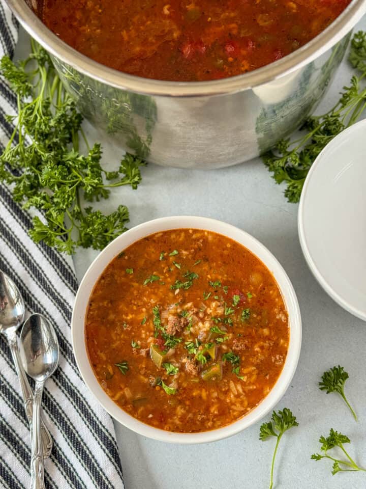 Bowl of instant pot stuffed pepper soup with spoon on the side all sitting in front of instant pot.