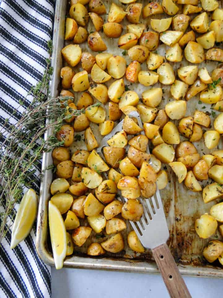 Lemon thyme roasted potatoes being served on spatula from sheet pan.