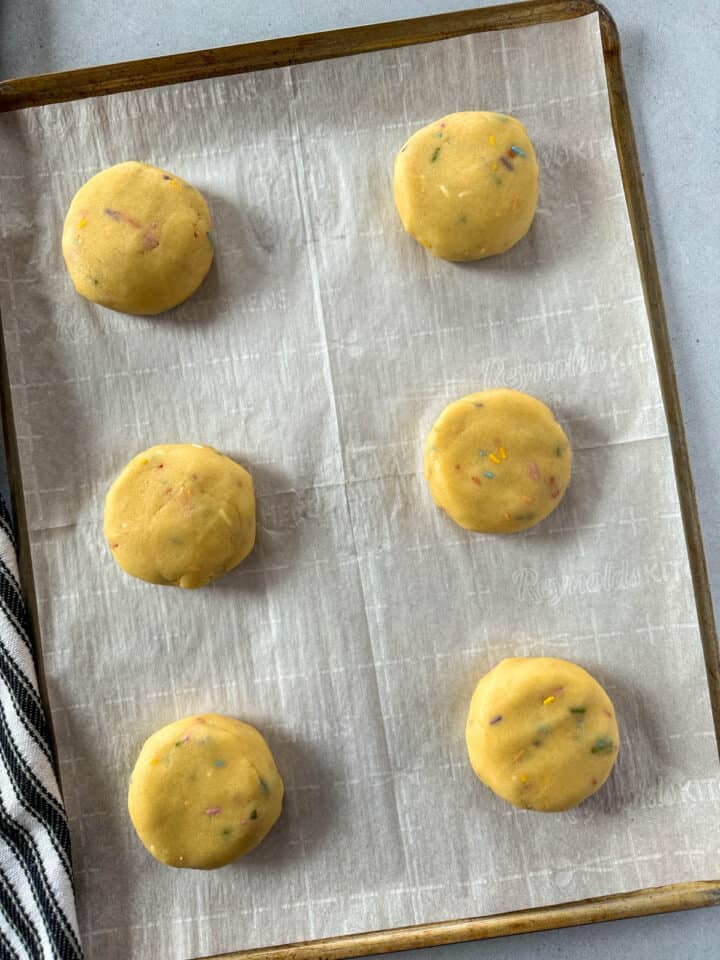 Six cookie dough pucks on cookie sheet with parchment paper.