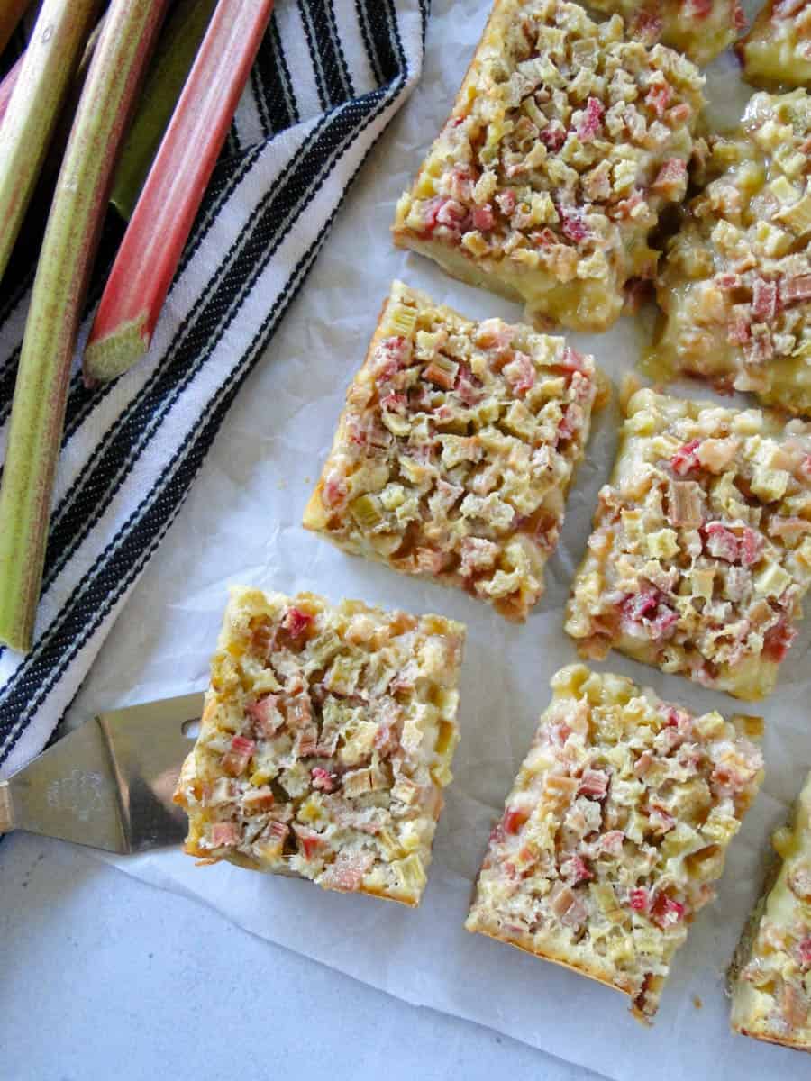 Six rhubarb custard bars in two columns with mini spatula under one bar and rhubarb stalks on the side.