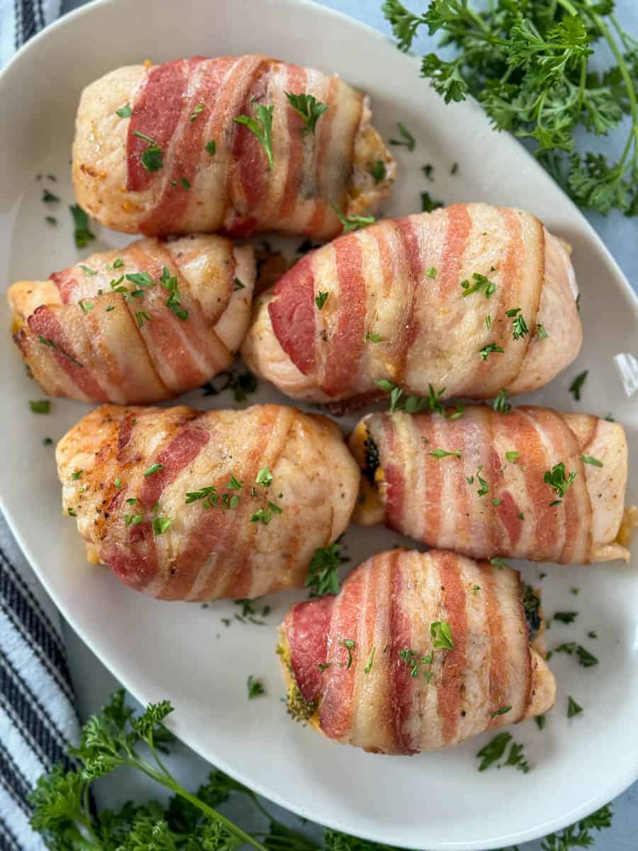 Top view of bacon wrapped cheesy broccoli chicken on white oval platter.