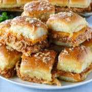 Side view of bbq chicken sliders piled on white round plate.