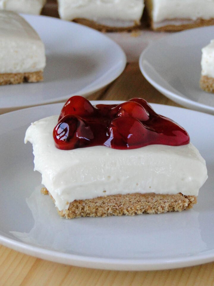 Close up side view of no bake cheesecake bar on white round plate topped with cherry pie filling.