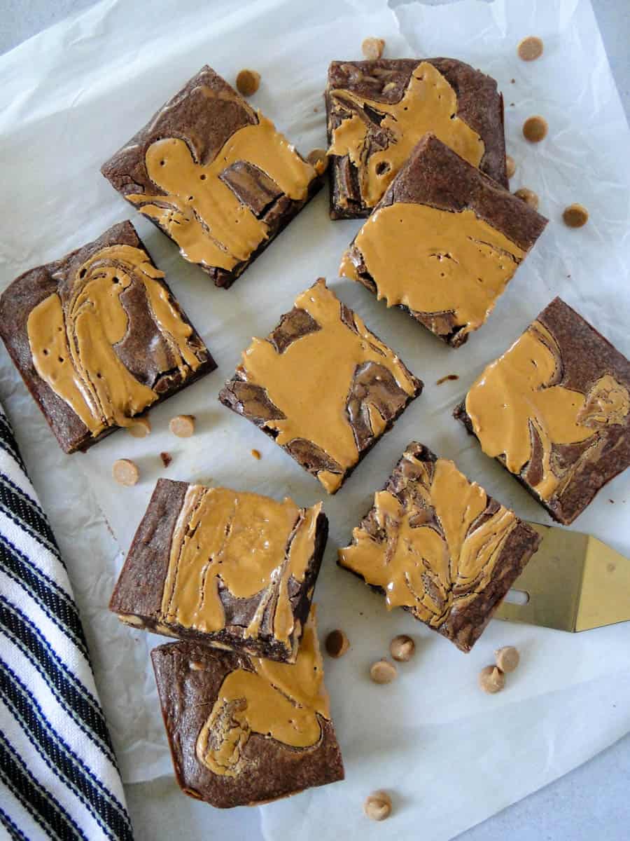 Peanut butter swirl brownies sliced and piled on parchment paper with spatula under one brownie.