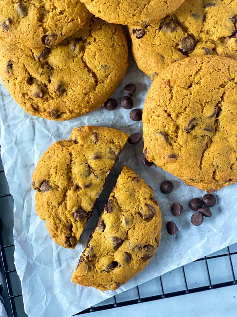 Top view of pumpkin chocolate chip cookies on parchment paper with one cookie cut in half.