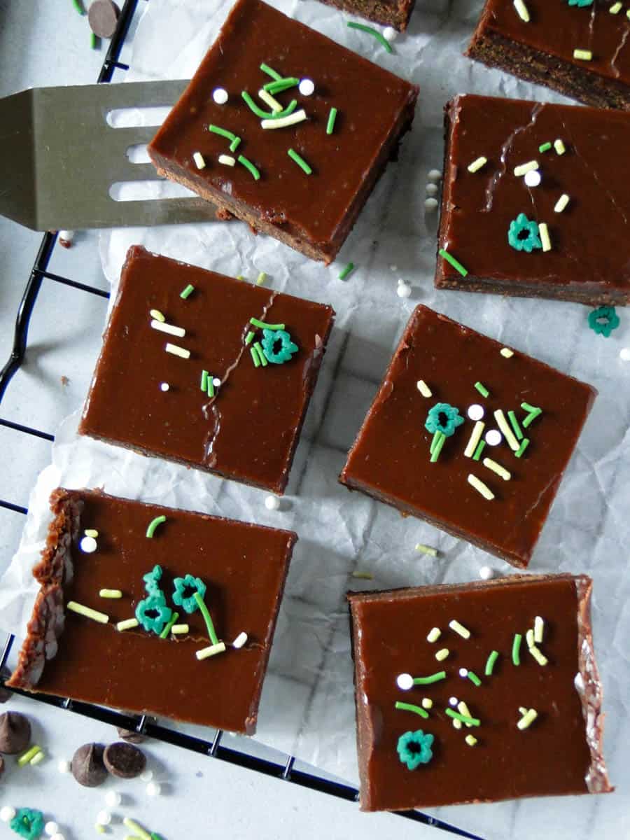 Top view of zucchini brownies with fast frosting on wire rack with spatula under one brownie.