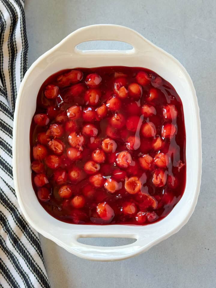 Cherry pie filling spread out in white square baking dish.