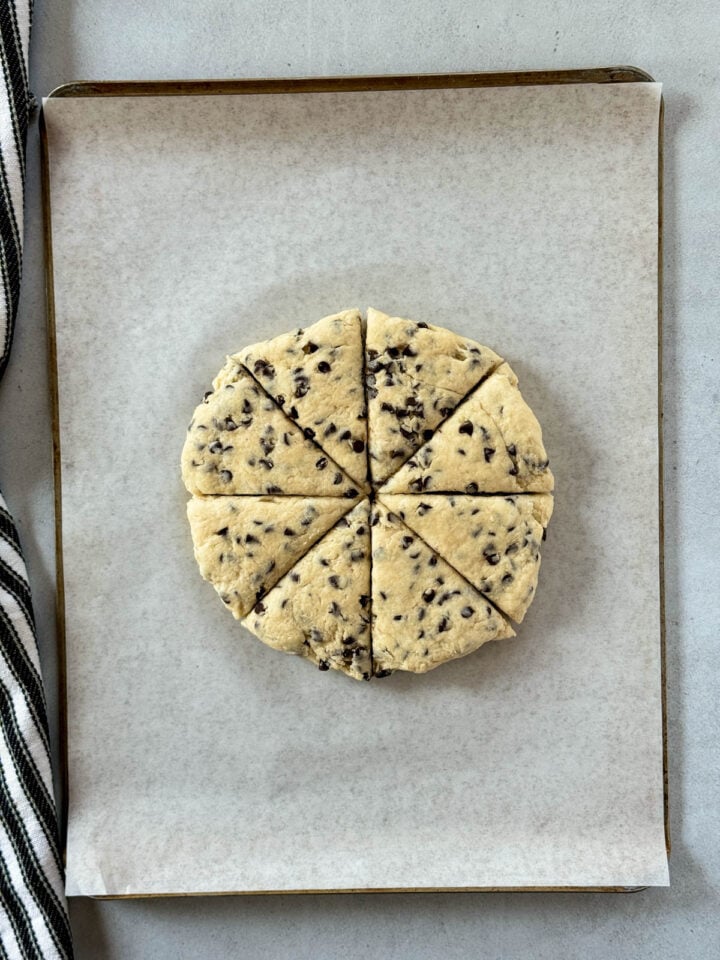 Scone dough pressed into circle and cut into 8 triangles on parchment lined sheet pan.