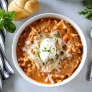 Lasagna soup in bowl topped with ricotta sitting in front of dutch oven with garlic bread to the side of bowl.