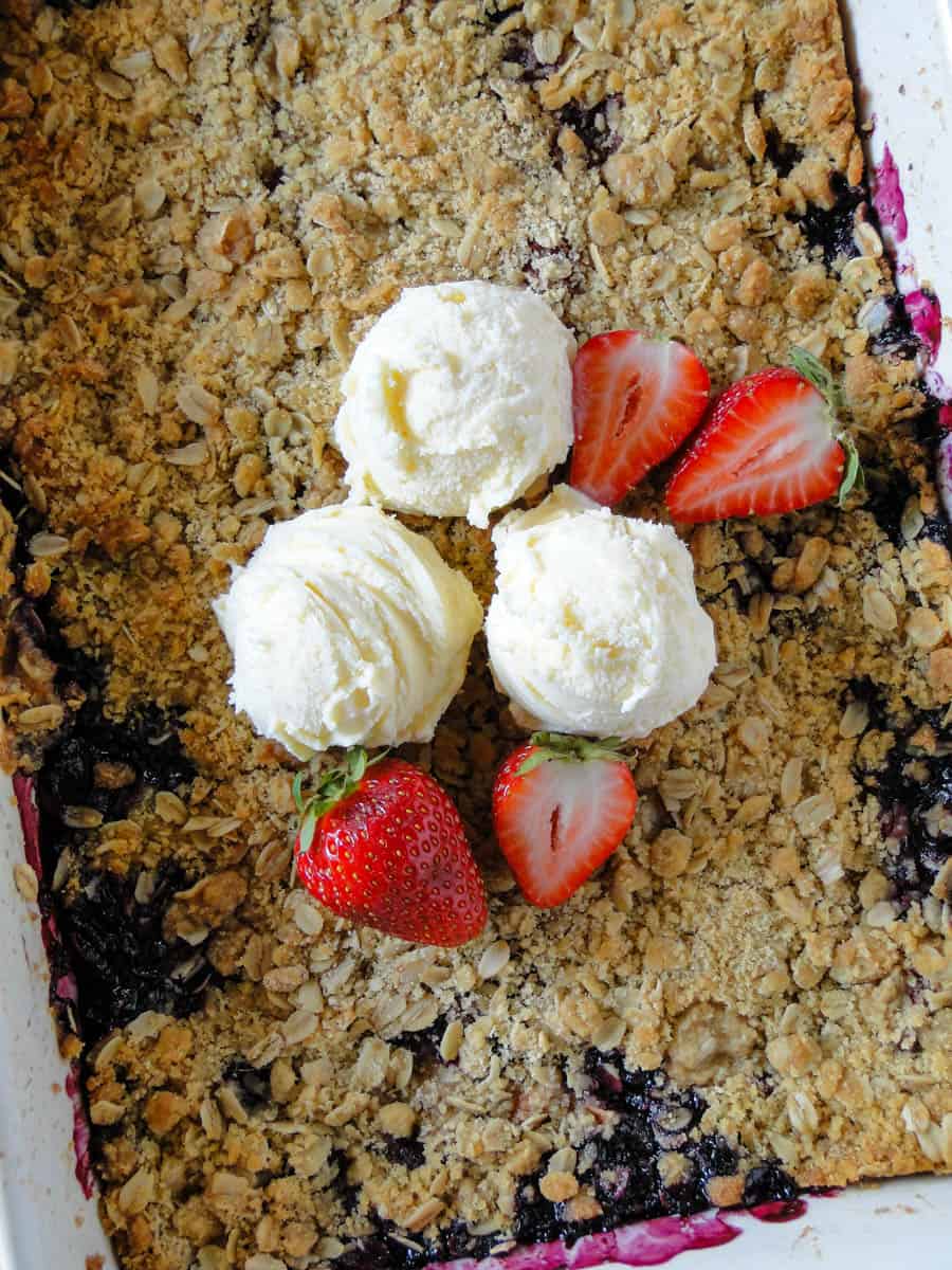 Close up top view of berry apple crisp in baking dish topped with 3 scoops of vanilla ice cream.