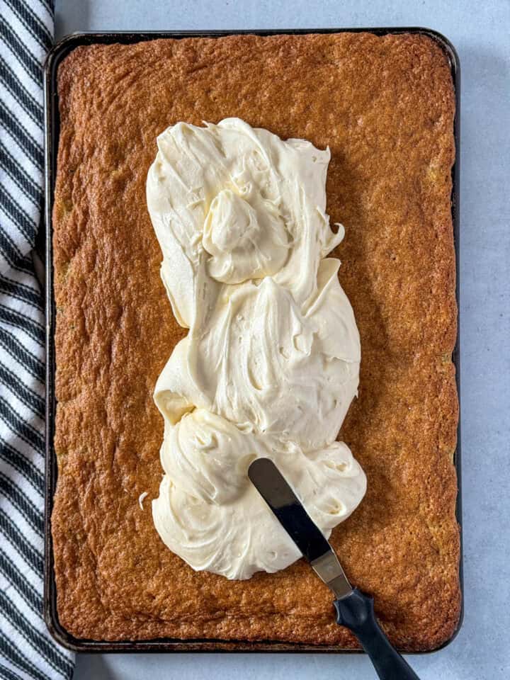 Cream cheese frosting piled in center of bars with offset spatula.
