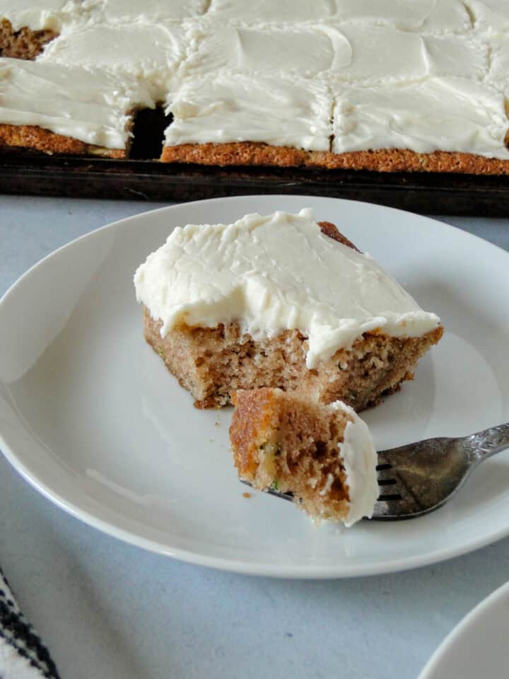 Side view of zucchini bar slice on white plate with bite on fork.