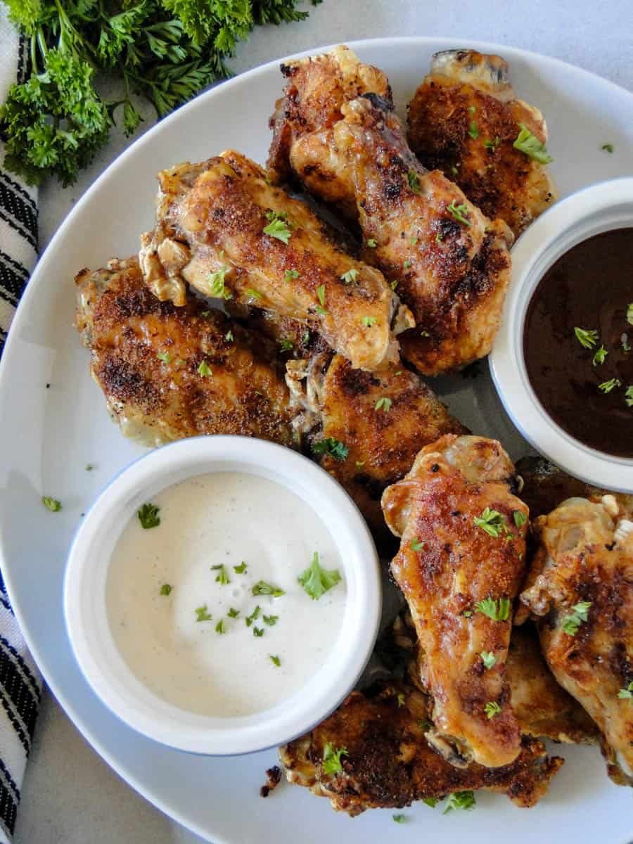Air fryer chicken wings on white plate with cups of sauces.