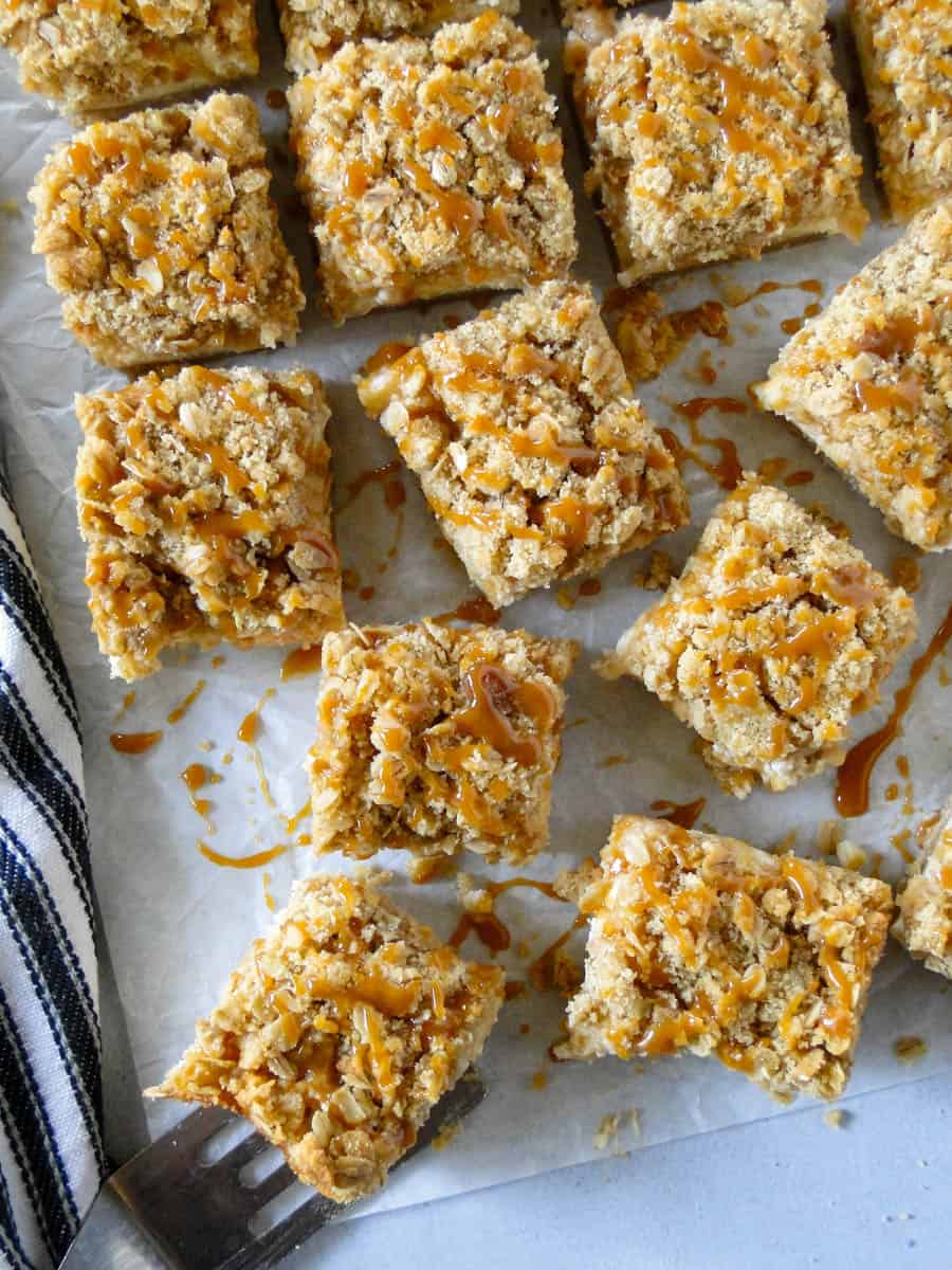 Top view of apple cheesecake streusel bars drizzled with caramel with one bar on top of spatula.