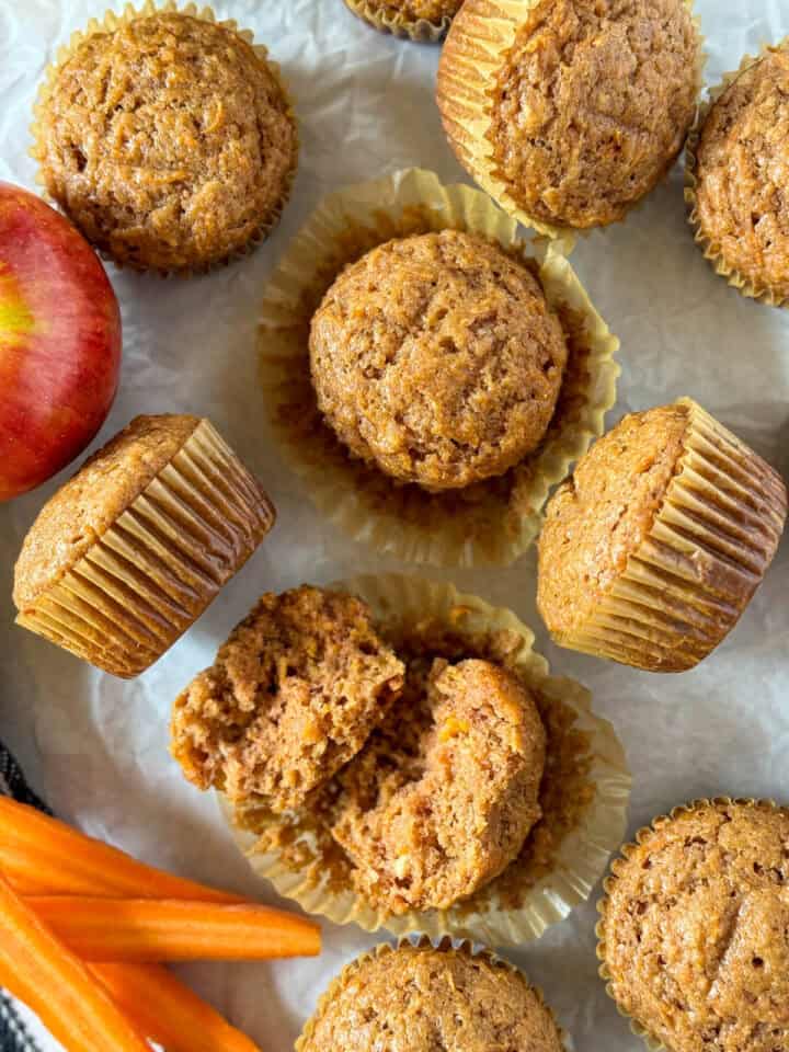 Top view of Applesauce Carrot Muffins on parchment paper with some turned on side and one broke in half.