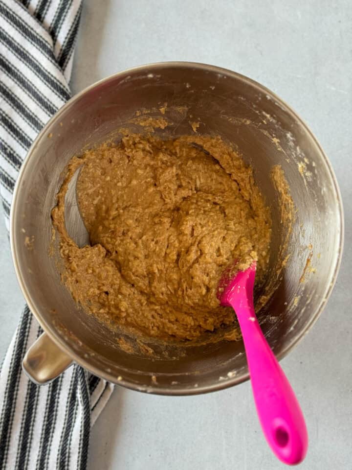 Dry ingredients added to wet in mixing bowl with pink spatula.