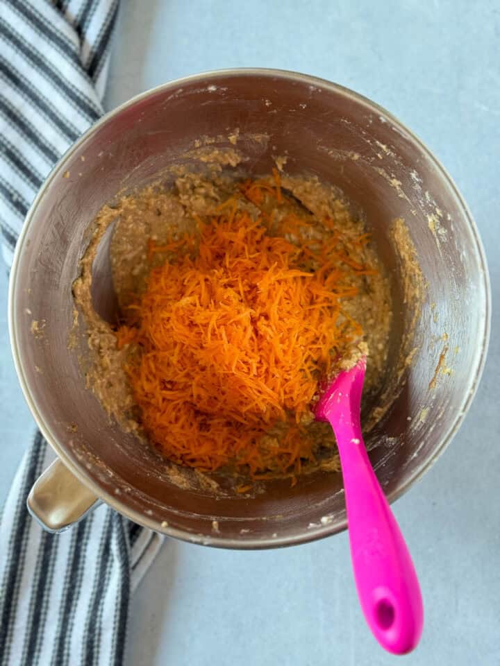 Carrots added to top of muffin batter in metal mixing bowl.