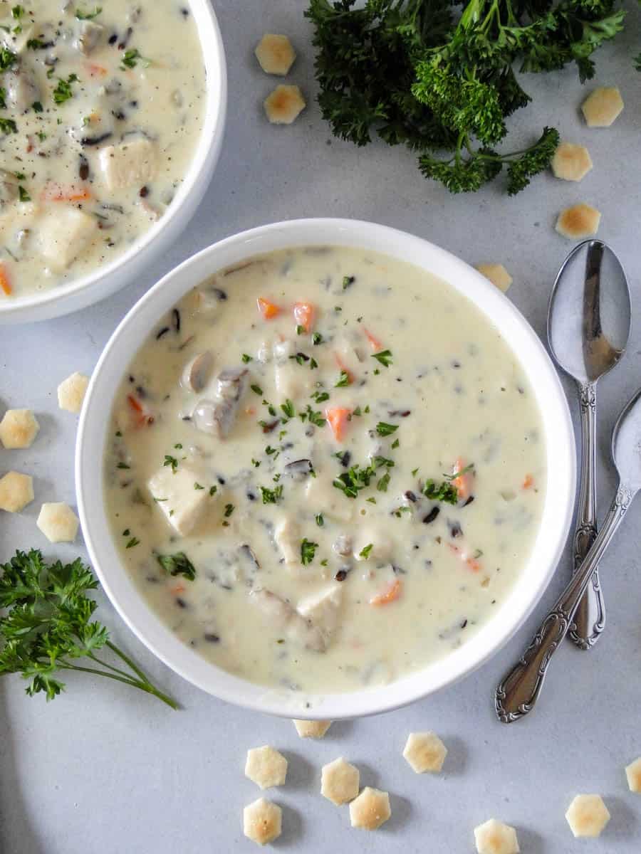 Bowl of chicken wild rice soup next to another bowl of soup with spoons on the side.