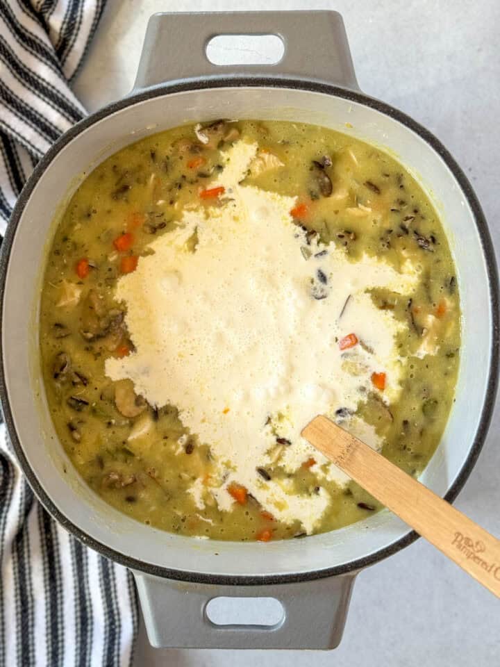 Cream added to soup in dutch oven with wooden spoon.