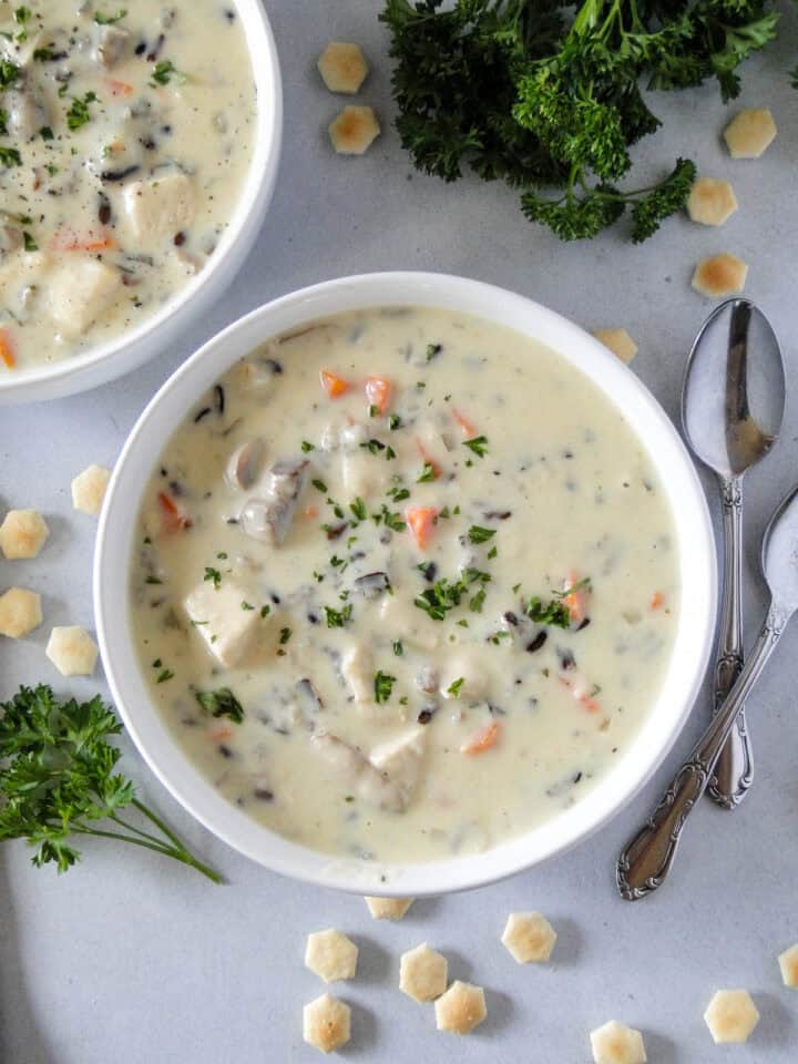 Bowl of chicken wild rice soup next to another bowl of soup with spoons on the side.