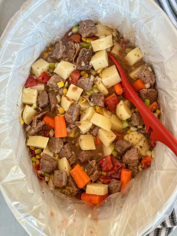 All ingredients stirred together in crock pot with red spoon.