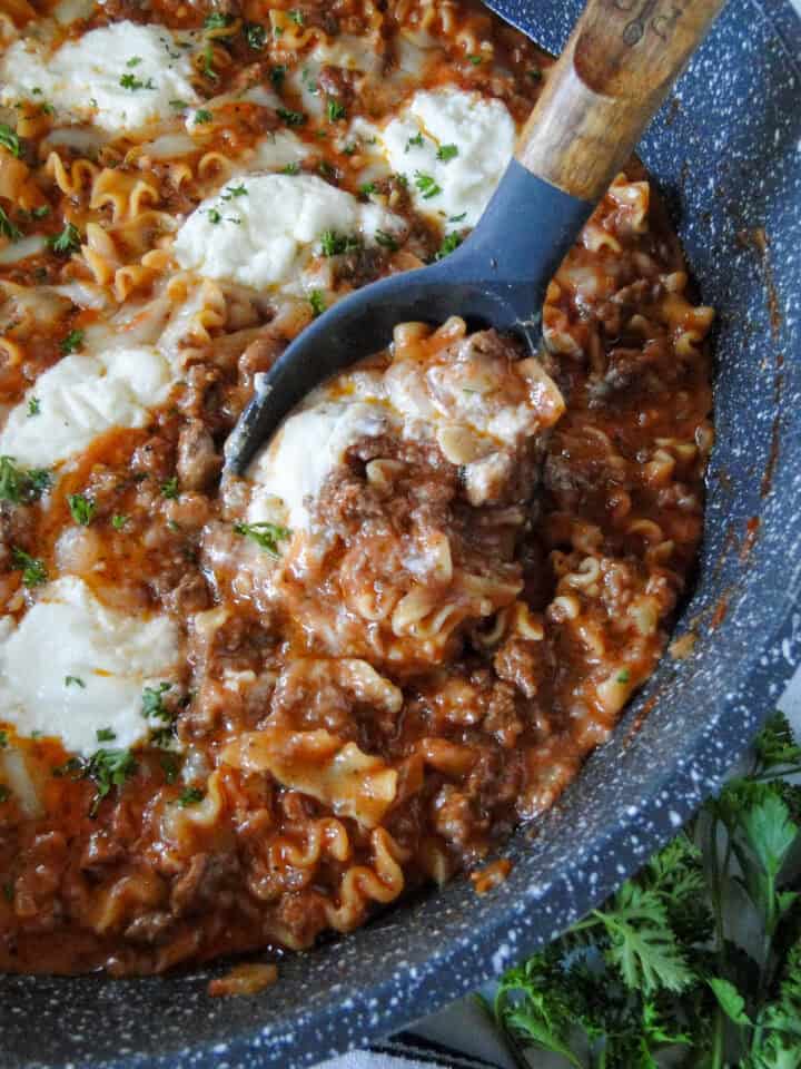 Easy lasagna skillet being scoop with serving spoon from top right of pan.