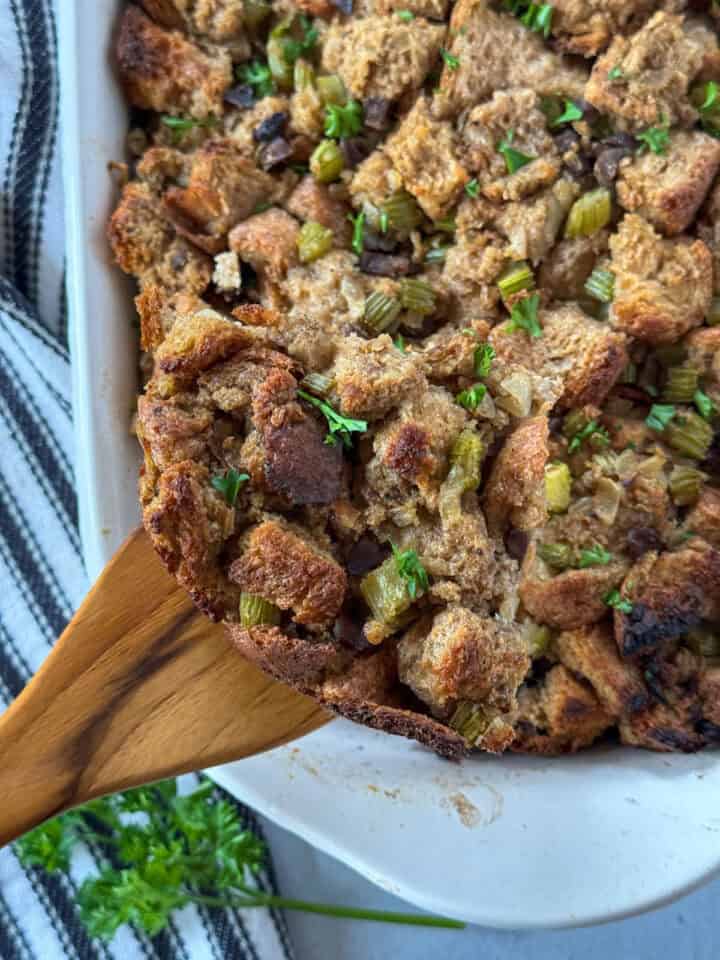 Top view of homemade stuffing being served out of casserole dish with wooden spoon.