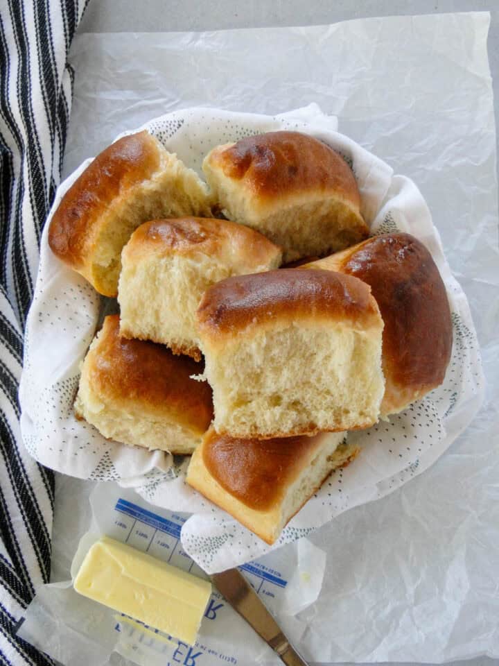 Top view of no knead dinner rolls piled into basket with stick of butter and bread knife on side of basket.