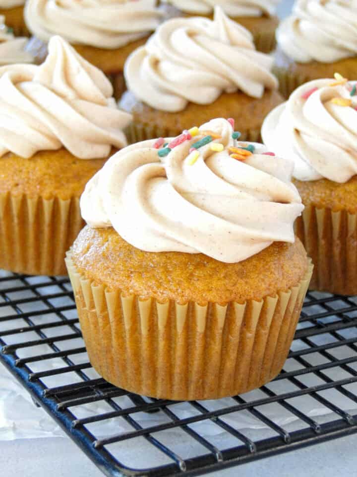 Side view of pumpkin cupcakes with cinnamon cream cheese frosting on wire rack.