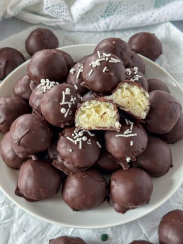 Chocolate coconut candy piled on white platter with one candy cut in half showing center.