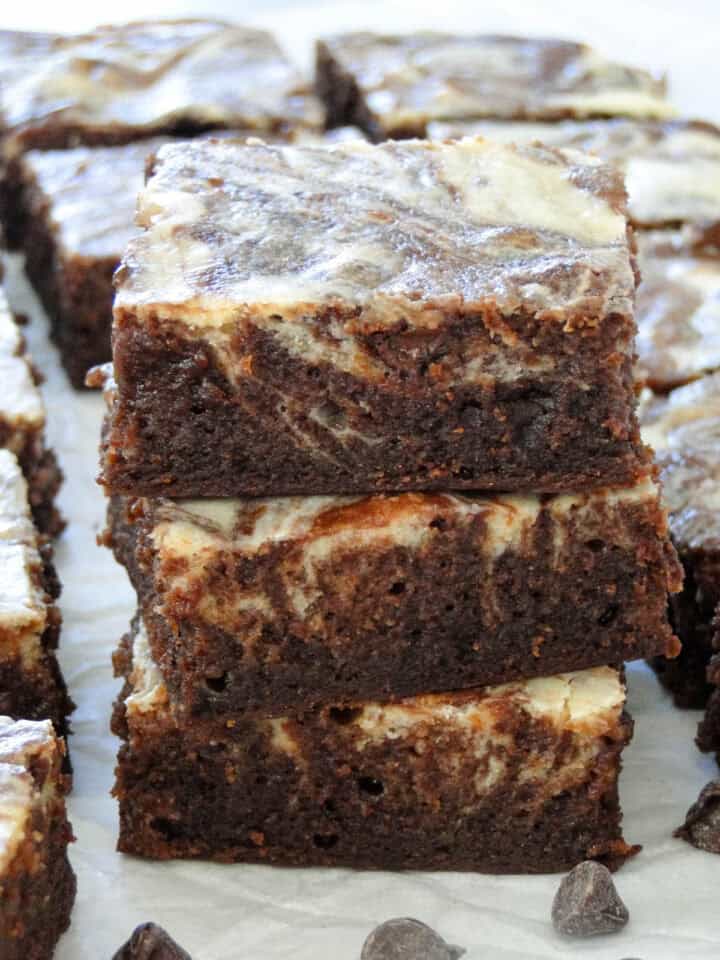 Close up side view of three cheesecake swirl brownies stacked in front of other brownies.