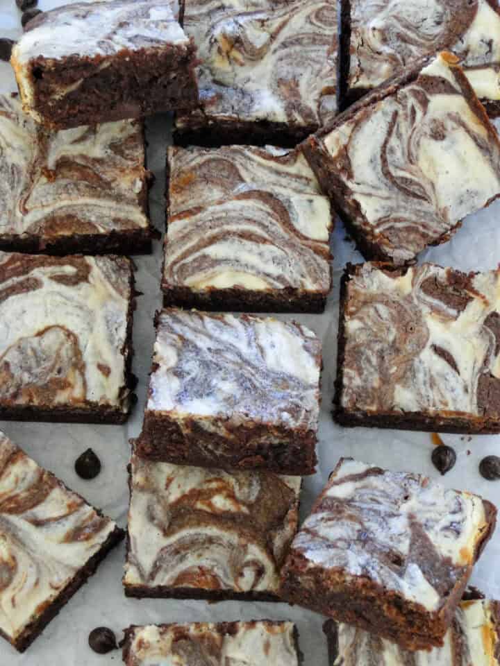 Top view of sliced cheesecake swirl brownies scattered and staggered on parchment paper.