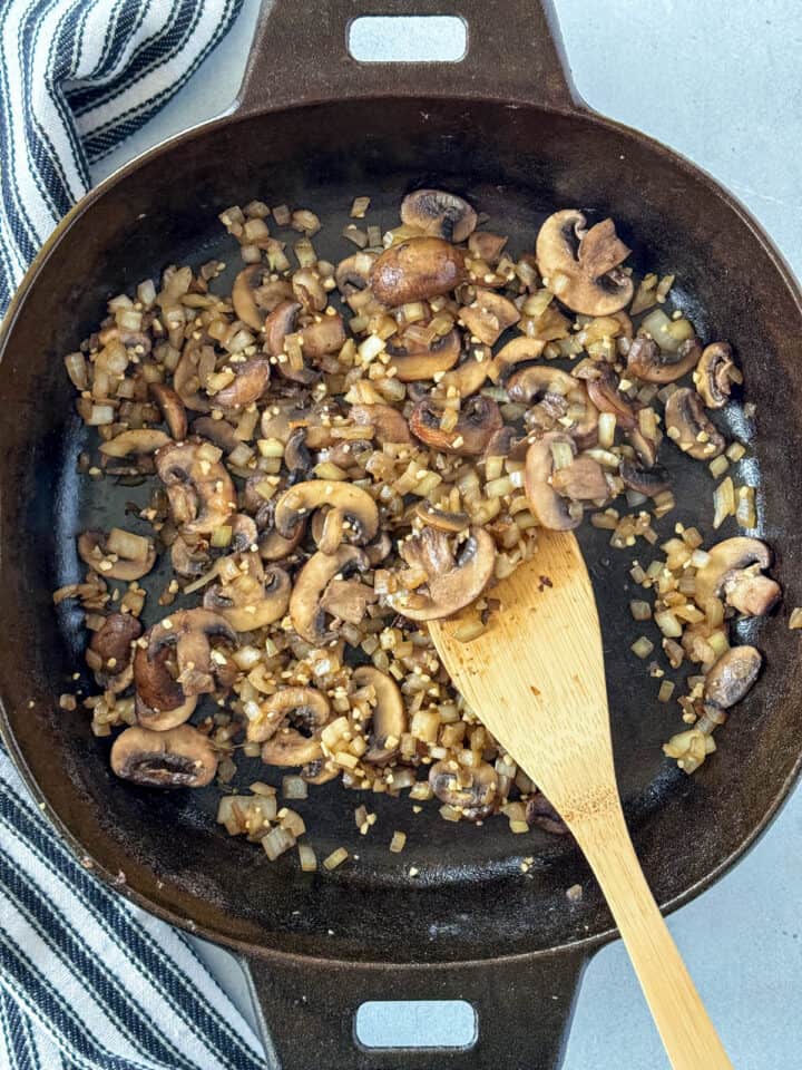 Cooked mushrooms and onions in cast iron skillet with wooden spoon.