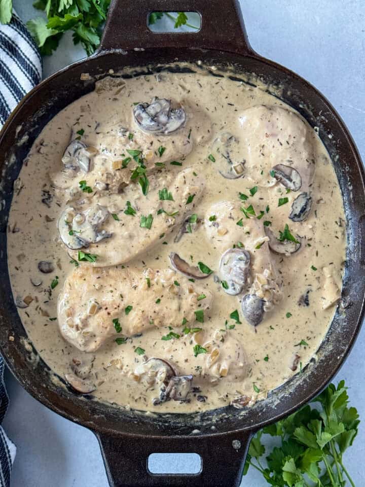 Chicken breasts added to mushroom sauce in cast iron skillet.
