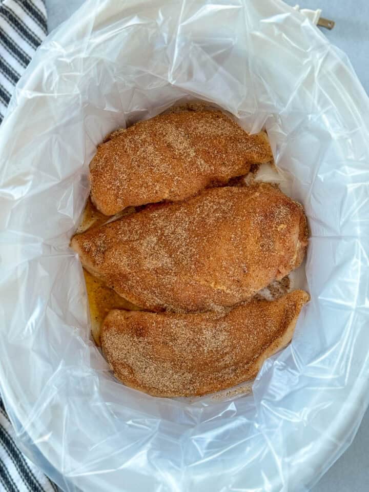 Spices sprinkled over chicken breast in crock pot.