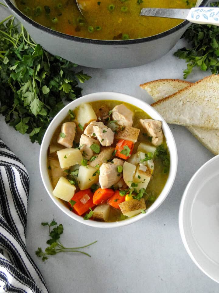 Chicken and potato stew in white bowl in front of dutch oven with ladle.