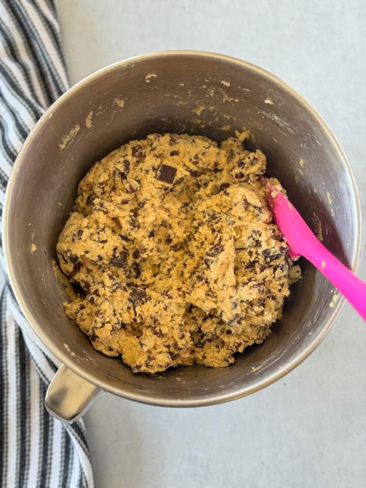 Cookie dough complete in metal mixing bowl with pink spatula.