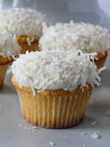 Close up side view of coconut cupcake in front of other cupcakes.