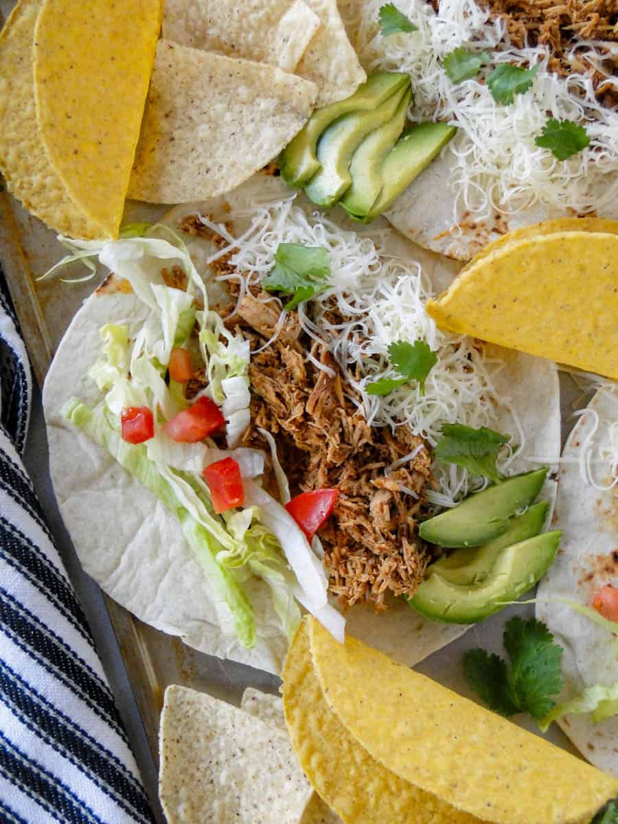 Crock pot chicken tacos made with flour tortillas laying flat with hard shells surrounding them.