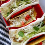 Top view of soft shell tacos filled with crock pot chicken taco meat on red taco plate.