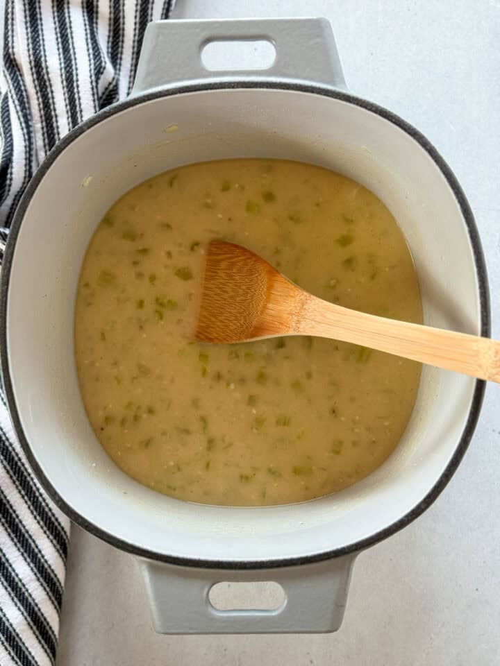 Broth added to sauteed veggies in dutch oven with wooden spoon.