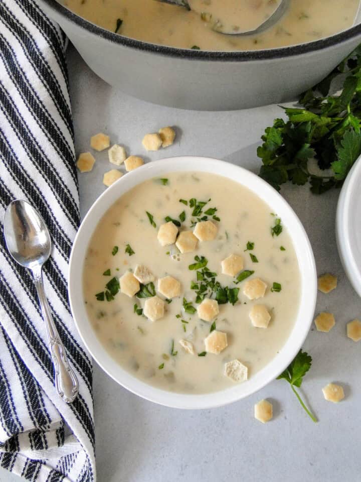 Top view of easy clam chowder in white bowl topped with oyster crackers sitting in front of dutch oven.