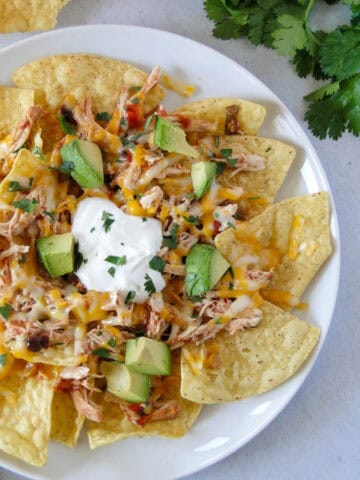 Instant pot salsa chicken nachos on white round plate.