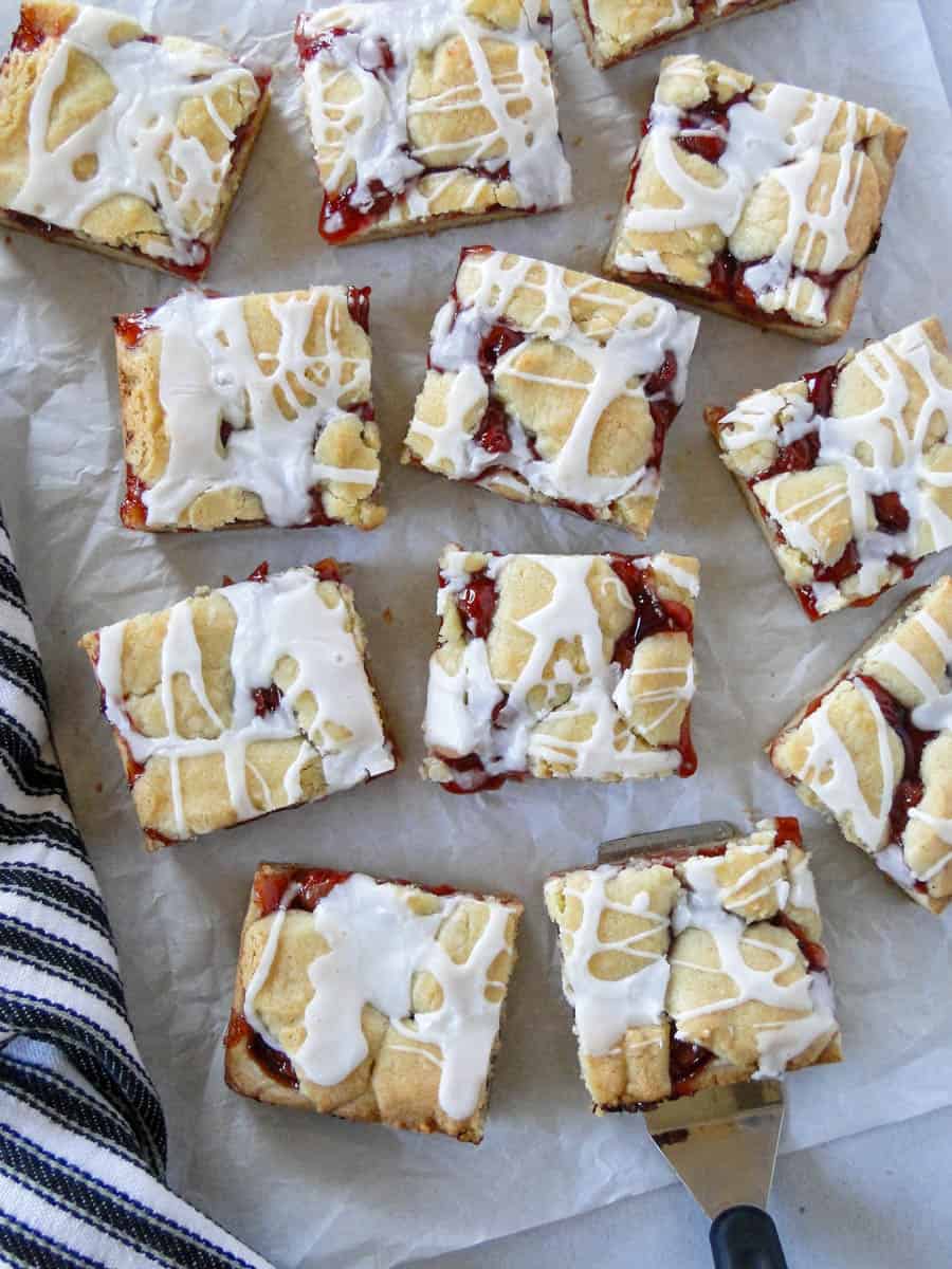 Top view of sliced cherry bars scattered on parchment paper and one cherry bar on spatula.